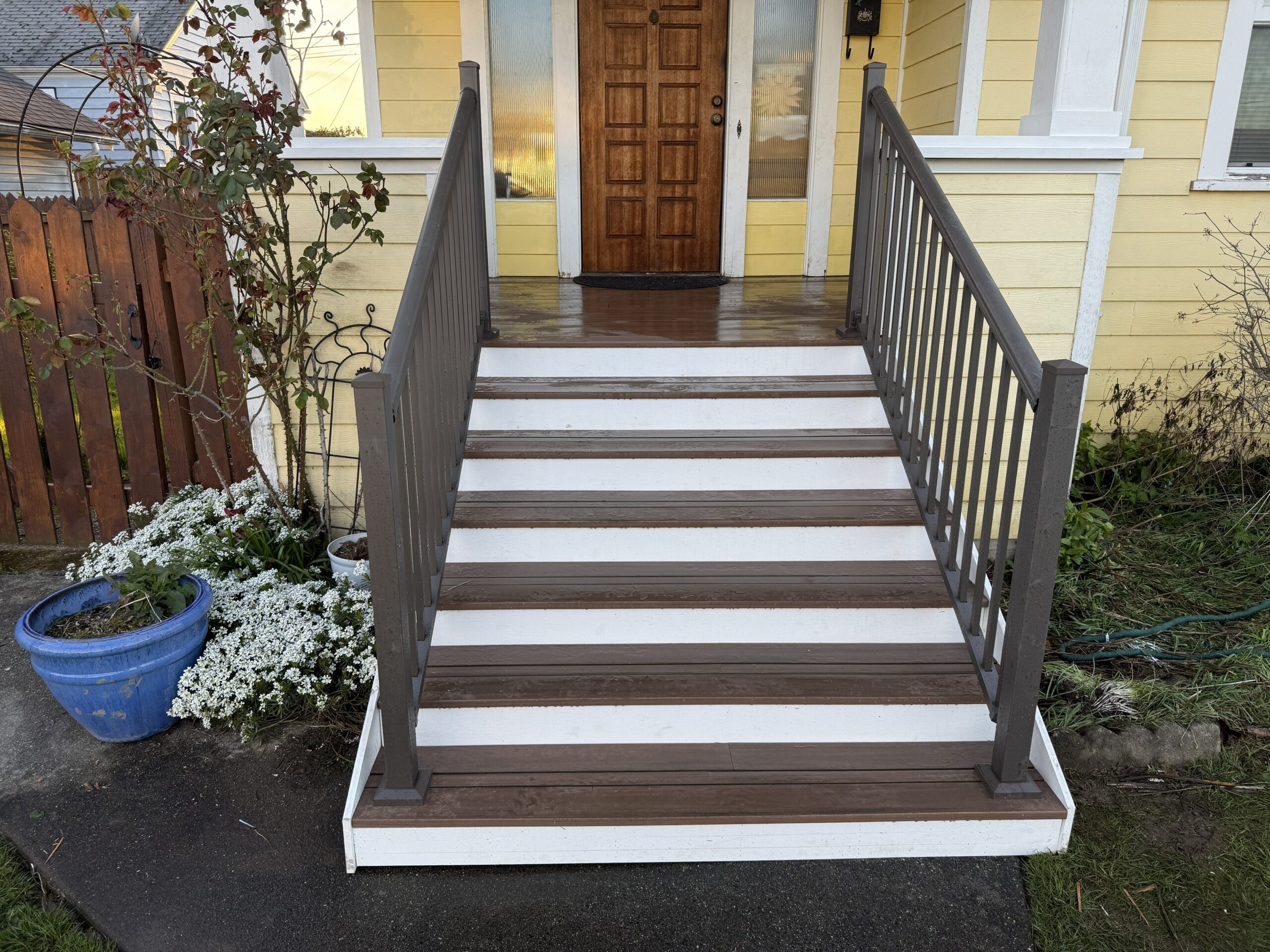Newly rebuilt front porch stairs with composite decking and gray metal railings leading to a home's front entrance.
