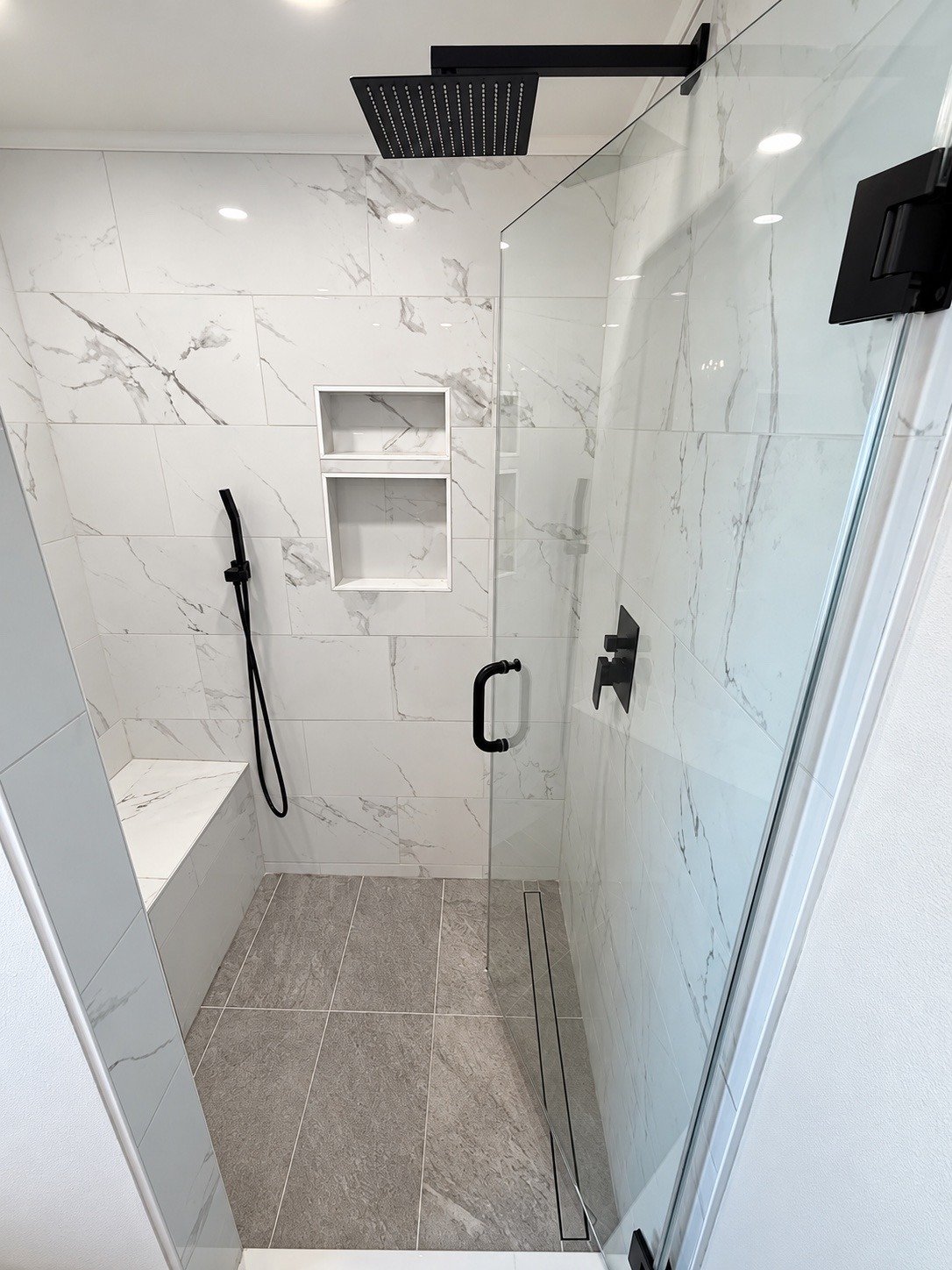 Prestige bathroom remodel with marble-look shower tile, glass enclosure, built-in bench, and black fixtures in Burlington